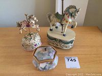 View of three music boxes on table including carousel horse, ornate horse on base, and butterfly painted trinket box