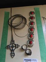Full view of all jewelry items showing cross pendant on a chain, bracelet with red stones, two rings, and several bangles.