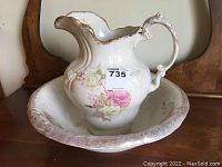 Front view of ceramic jug sitting inside matching bowl showing floral decoration and gold trim detailing.