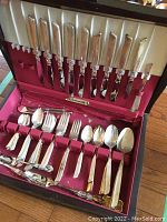 Full view of open flatware canteen showing knives in the lid and various forks, spoons, and serving pieces in the base tray lined with red velvet.