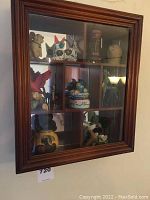 Wall mounted wood-frame curio cabinet with glass front and mirror backing, showing various small figurines inside compartments