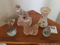 Overview of all five decorative items on a wooden surface showing the Belleek vase, the Waterford butterfly, the Cristal d'Arques cat, and two glass paperweights.