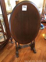Oval wooden side table standing upright folded with visible base and turned legs