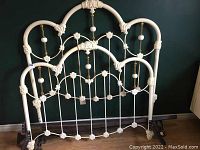 Front view of the full size metal bed frame showing the headboard standing upright against a wall with visible ornamental floral and spherical elements.