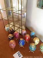 Eleven hand-painted decorative ornamental eggs in various colors and gold accents displayed in front of the cabinet.