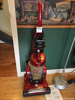 Full view of upright Hoover vacuum cleaner with red body and transparent dirt cup, showing overall appearance and size.