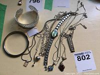 Full view of assorted silver colored jewelry including cuff bracelet, bangle, multiple necklaces, and wristwatch