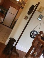 Wooden coat stand with metal hooks, leather hat hung on it, located in a room with tiled floor and kitchen appliances in background