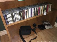 Wide shot showing collection of music CDs in jewel cases on a shelf, Sony Discman and carrying case on lower shelf.