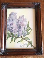 Full view of framed watercolour painting showing purple lilac flowers on green leafy branch, signed and dated, with decorative wooden frame.