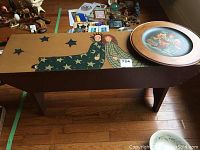 Side view of the painted wooden bench with folk art figures under stars and surface wear visible.