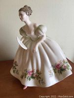 Front and side view of the Royal Doulton Samantha figurine showing the figure holding a fan, with detailed floral pattern on the dress.