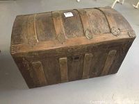 Front view of small vintage steamer trunk highlighting wooden slats, metal hardware and worn patina.