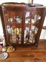Front view of solid wood display cabinet with glass paneled doors revealing interior shelves displaying china dishes and collectibles.