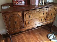 Front angle view of solid wood sideboard showing drawers and cabinet doors with brass handles and scalloped apron.
