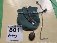 Sterling silver locket pendant, sterling silver chain necklace, and a sterling silver bracelet displayed on a green velvet pouch on a wooden surface.