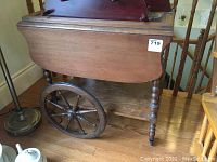 Side view of the wooden tea cart showing the turned legs, large spoked wheel and bottom shelf.