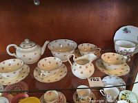 Wide view of tea set including teapot, creamer, four cups and saucers, and small bowl on display shelf.