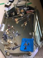 Photo showing assortment of cuff links, hat pins, watches, earrings on a vintage mirror tray