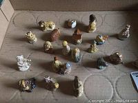 21 Wade miniature porcelain figurines arranged in a cardboard container, showing a variety of animals, people, and objects. Good condition from a smoking home with possible chips or cracks.