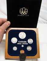Opened hardwood box showing all seven coins displayed in blue felt with Canadian Olympic logo on lid.