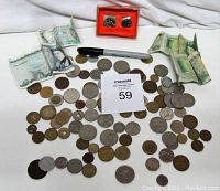 Overview of approximately 95 coins, notes, and tokens spread out with a marker for scale and a boxed set of Israeli coins with orange backing.