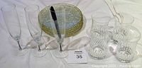 Full lot showing 3 champagne flutes, 5 dessert plates with gold trim stacked, 4 water glasses with lead crystal cut pattern all arranged on table.