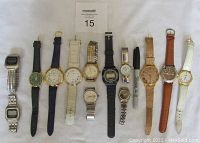 Overview of 13 assorted wristwatches laid out horizontally showing variety of strap types and watch faces.