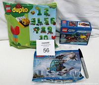 Photo showing three Lego kits: LEGO Duplo 40304 sealed in green plastic bag, LEGO City 60090 boxed set, and LEGO City 30351 sealed polybag with a pen showing scale.