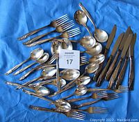 Full lot spread out on blue cloth including forks, knives, spoons, and serving spoons.