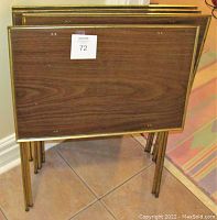 Stacked view of four vintage Mid Century Modern collapsible TV or side tables showing wood grain tops and brass-colored metal frames folded flat for storage.