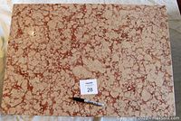 Top view showing the pink and light brown mottled marble slab tabletop with a marker and lot number card for scale.
