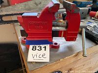 Red bench vise mounted on wooden workbench with model number 1033 and Colombian brand embossing