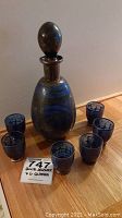 Blue glass decanter with stopper and six matching blue glasses arranged around it on a wooden surface, showing overall lot contents.