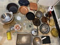 Overview of cast iron pans, copper pans, glass lids, mixing bowls, and miscellaneous cookware including a Bundt cake pan.