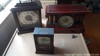 Three vintage clocks including Seth Thomas, University of Colorado, and smaller clock, displayed side by side on table