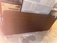 Photo of wood grain folding table in folded position leaning against wall.