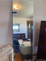 Full length rectangular mirror with beveled edges, reflecting bedroom furniture and wall fixtures.