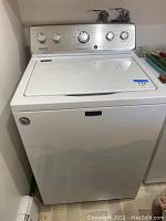 Front view of white Maytag washing machine with lid closed, showing exterior cabinet and control panel