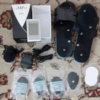 Full lot overview including eMP10 unit, therapy sandals, electrode pads, charger, and cables on carpet.