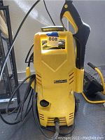 Front view of a yellow Karcher electric power washer with attached spray gun and power cord.