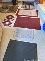 Assortment of nine small rugs arranged on flooring including patterned and solid colors.