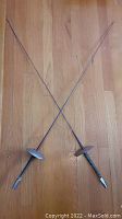 Pair of vintage French fencing rapier swords crossed on a hardwood floor showing overall condition and size.