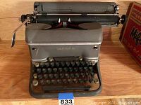 Full front and top view of vintage Smith Corona typewriter on wood surface showing carriage return lever and paper feed roller.