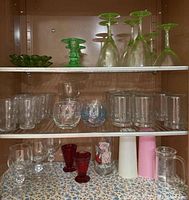 Shelf with two green depression glass martini glasses, four green wine glasses, four green candlestick holders, clear medium-sized glasses with star patterns, and small juice glasses.