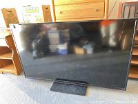 Front view of Vizio 65 inch TV showing black screen on stand in garage setting.