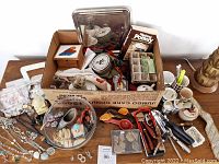 Full view of assorted used items, displaying the full contents of the box and surrounding miscellaneous objects such as jewelry and tools