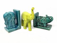 Front angle view of three ceramic elephant items: two turquoise elephant bookends with detailed carvings and one chartreuse elephant figurine with raised trunk.