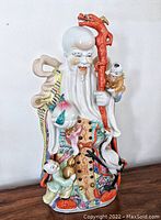 Front full view of the colorful hand-painted porcelain statue of Shou Xing, showing all details including red staff with dragon, peach, long beard, and accompanying figures.
