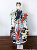 Front view of colorful ceramic/porcelain statue representing Lu Xing, Chinese God of Prosperity, standing with two children and holding red scroll.